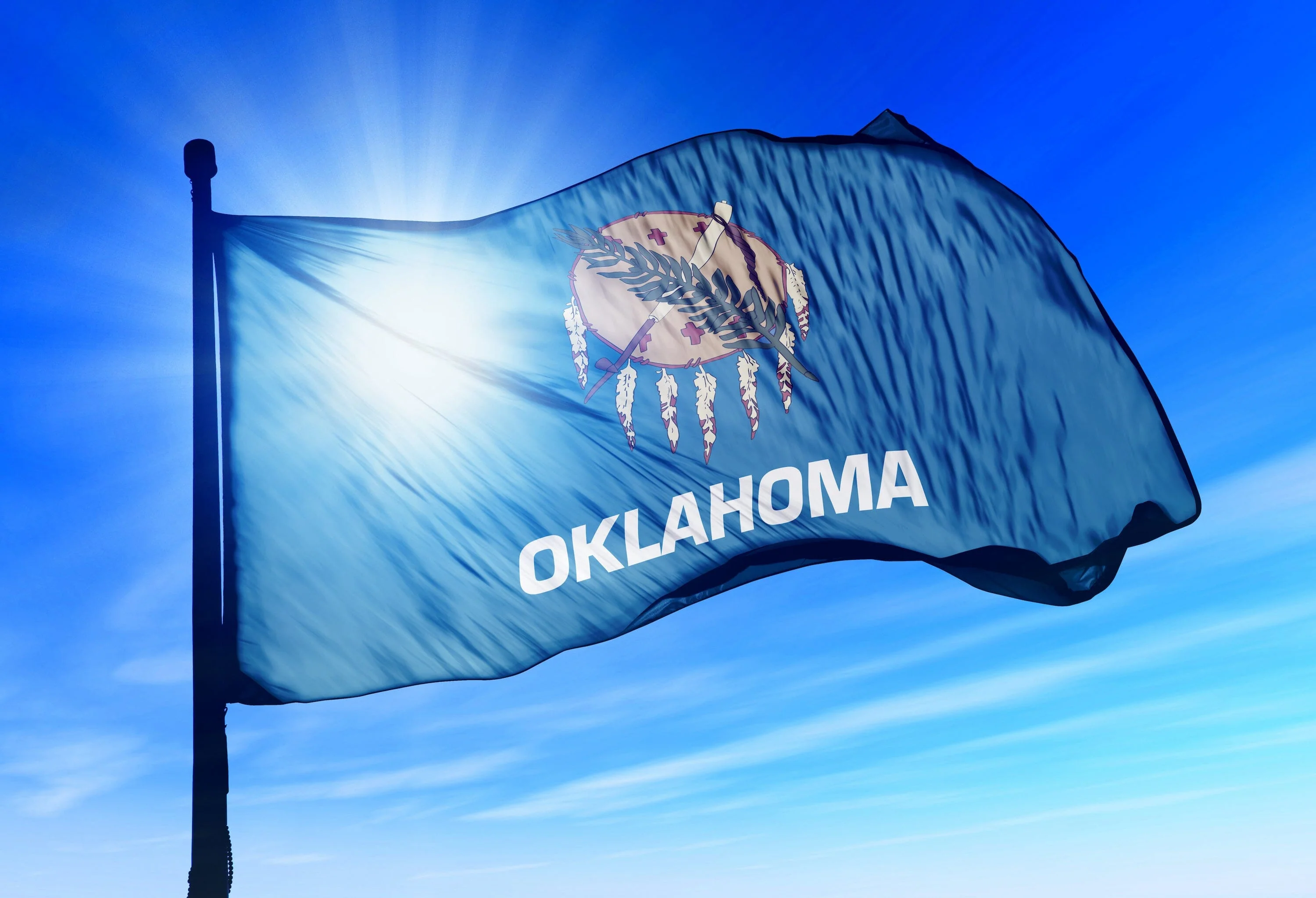 The Oklahoma state flag flying against a bright blue sky