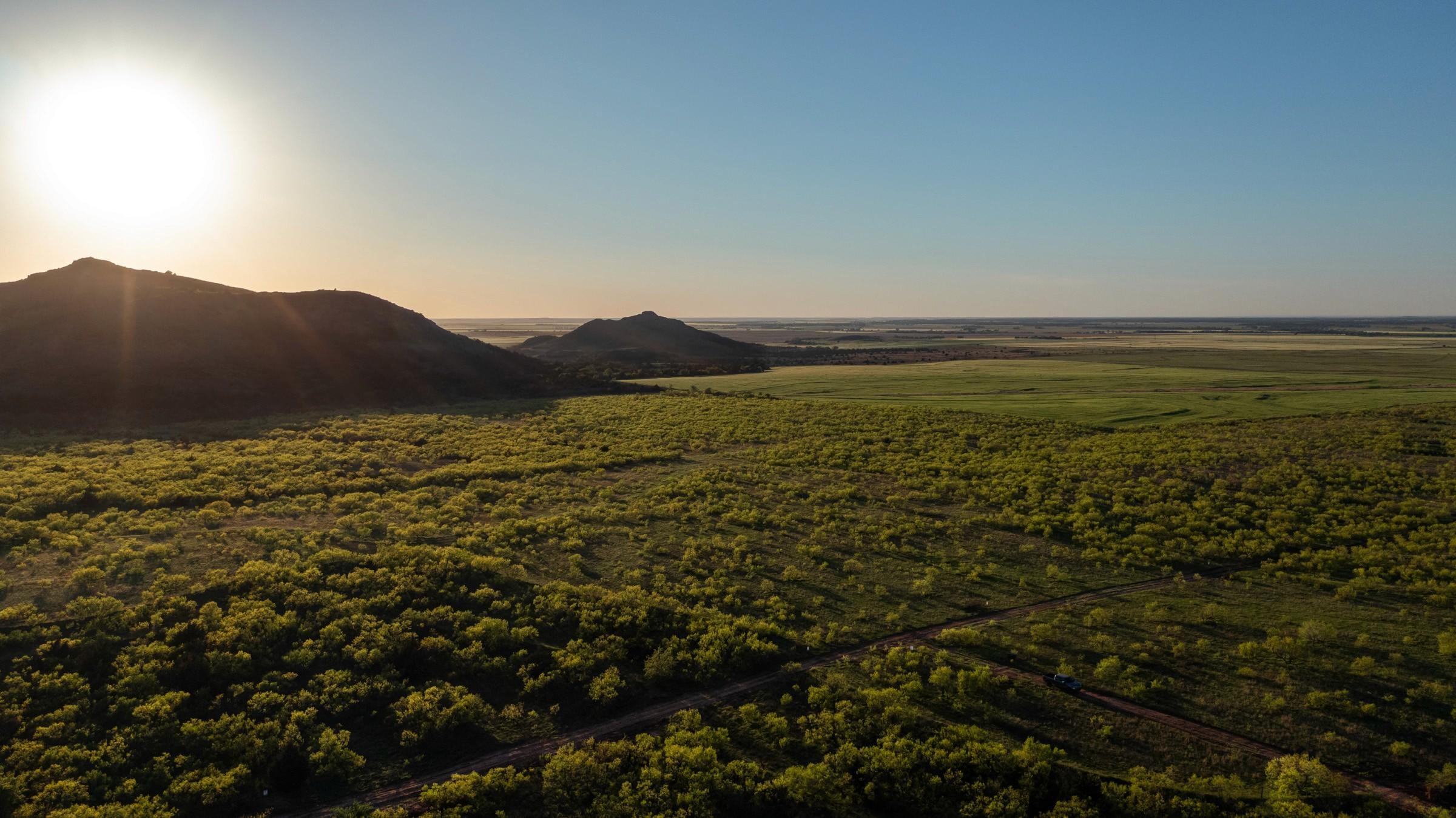 Sun low over granite hills beyond green scrub on rural Greer County, Oklahoma land