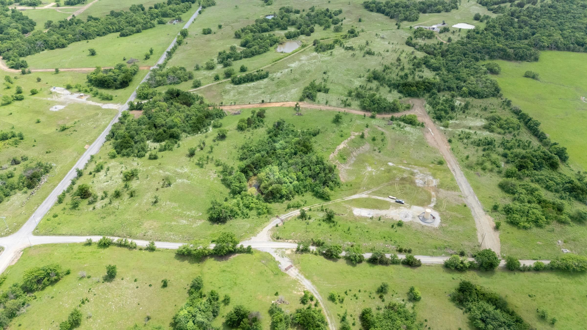 Aerial view of green rolling pasture and scattered timber in Pittsburg County, Oklahoma, crossed by dirt roads and cleared ground