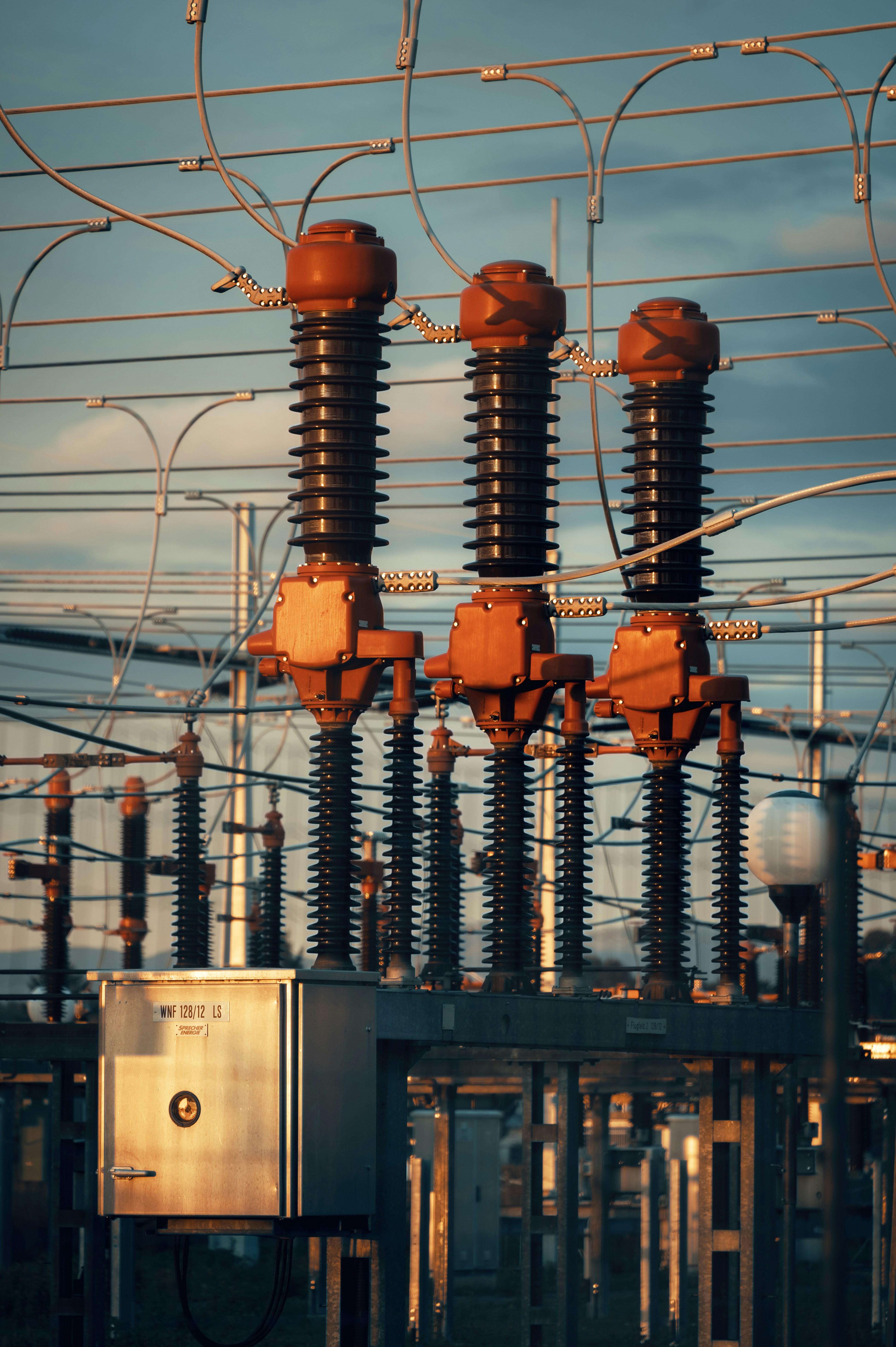High-voltage switches and insulators at an electrical substation, lit by low evening sun