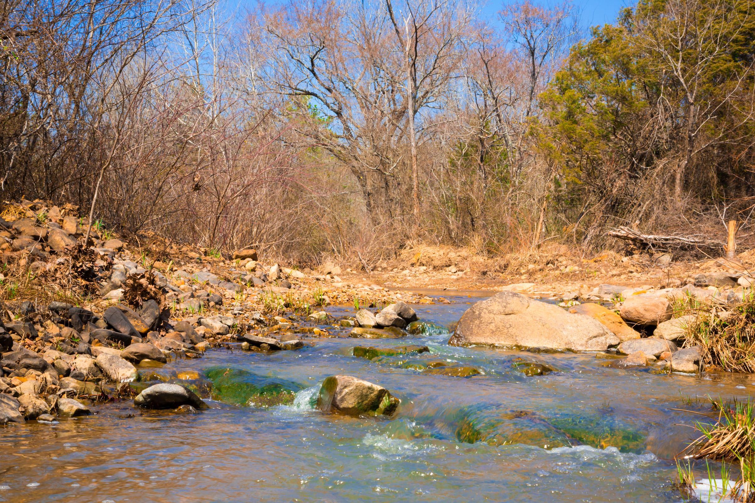 A clear, shallow creek running over rock between banks of bare winter trees in Latimer County, Oklahoma
